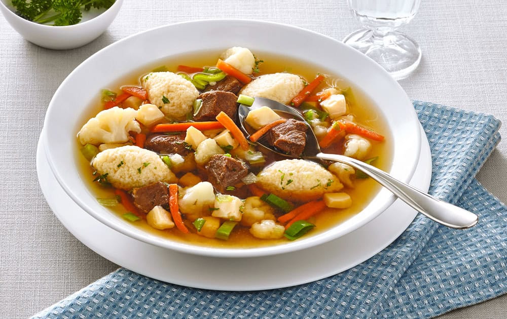 Gem&uuml;sesuppe auf einem wei&szlig;en Teller mit frischen Zutaten.
